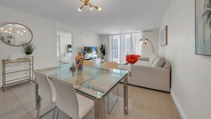 A modern living room with a glass dining table, white sofas, and a large mirror.