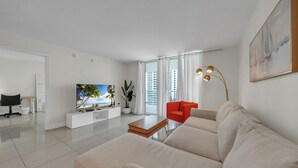 A modern living room with a sofa, a coffee table, a TV, a plant, and a painting on the wall.