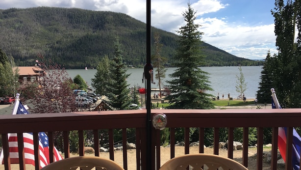 A deck with two chairs, a flag, and a view of a lake and forest. - Lake Front Rental/Downtown Grand Lake
Apt 3 The Falcon (Grand Lake)