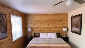 A cozy room with wooden walls, a bed with a colorful quilt, two bedside lamps, and a framed picture on the wall. - Lake Front Rental/Downtown Grand Lake
Apt 3 The Falcon (Grand Lake)