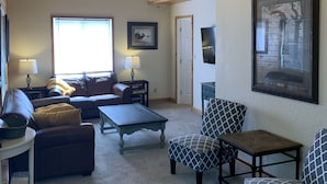 A cozy living room with a wooden ceiling, a sofa, a coffee table, and a patterned armchair. - Lake Front Rental/Downtown Grand Lake
Apt 3 The Falcon (Grand Lake)