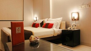 Una habitación de hotel con cama, mesita de noche, lámpara y una carpeta roja sobre la mesa.