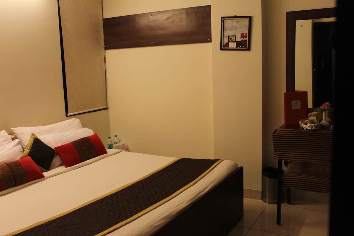 A neatly made bed with pillows, a bedside table with a vase and a bottle, and a mirror on the wall.