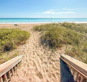 A sandy beach path with wooden railings leading to the ocean.