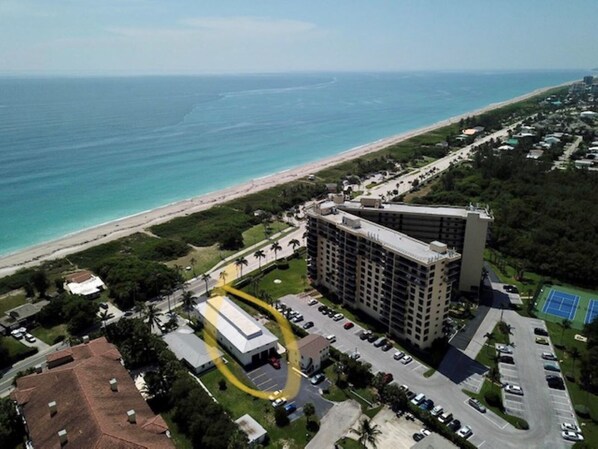 An aerial view of a hotel with a beach view, parking lot, and a tennis court.