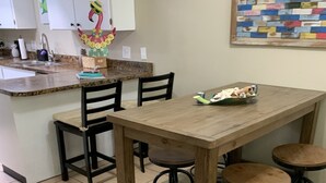 Una cocina con una mesa de madera, cuatro taburetes, un tapete y un adorno de pared colorido.