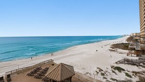 A beach with a sandy shore, a clear blue sky, and a building with balconies overlooking the beach. - Treasure Island 0412 (Panama City Beach)