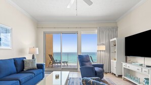 Ein modernes Wohnzimmer mit einer Couch, einem Sessel und einem Fernsehmöbel. Es gibt einen Balkon mit Meerblick.