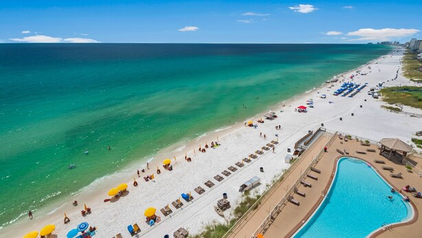 A beach resort with a swimming pool, sun loungers, and umbrellas.
