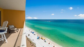 A balcony with a view of a beach, white chairs, and umbrellas.