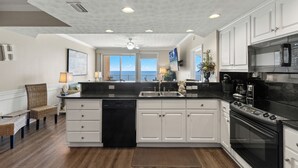 A kitchen with white cabinets, a black stove, and a view of the ocean. - Treasure Island 1009 (Panama City Beach)