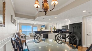 A modern kitchen with a black refrigerator, white cabinets, and a dining area with a glass table and black chairs. - Treasure Island 1009 (Panama City Beach)