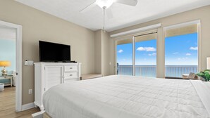 Een slaapkamer met een bed, een televisie, een plafondventilator en een balkon met uitzicht op de oceaan.