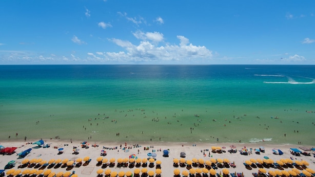 Een strand met rijen ligbedden en parasols, een heldere blauwe lucht en de oceaan.