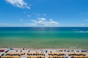 Ein Strand mit Reihen von Liegestühlen und Sonnenschirmen, einem klaren blauen Himmel und dem Meer.