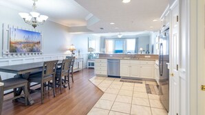 Une cuisine moderne avec des meubles blancs, un grand îlot central et un coin repas comprenant une table et des chaises en bois.