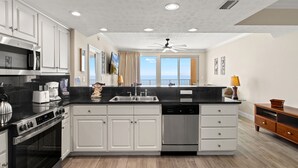 A modern kitchen with white cabinetry, a black countertop, stainless steel appliances, and a view to the outside. - Treasure Island 1208 (Panama City Beach)