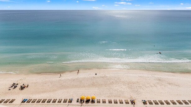 A beach with clear skies, calm sea, and sun loungers along the shore. - Treasure Island 1208 (Panama City Beach)