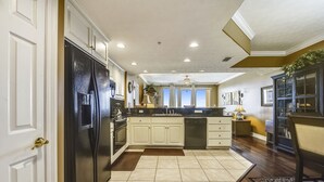 A spacious kitchen with white cabinets, a black refrigerator, and a wooden floor. - Treasure Island 2202 (Panama City Beach)