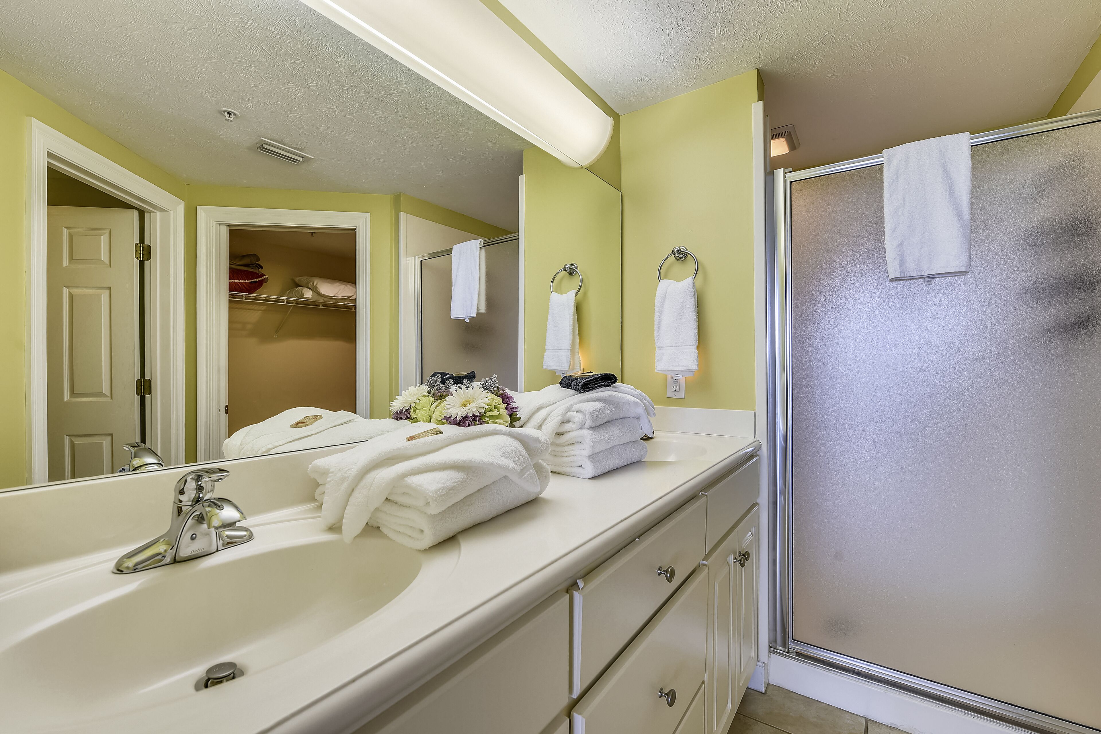 A bathroom with a large mirror, a white sink, a shower with frosted glass doors, and a towel rack with folded towels.