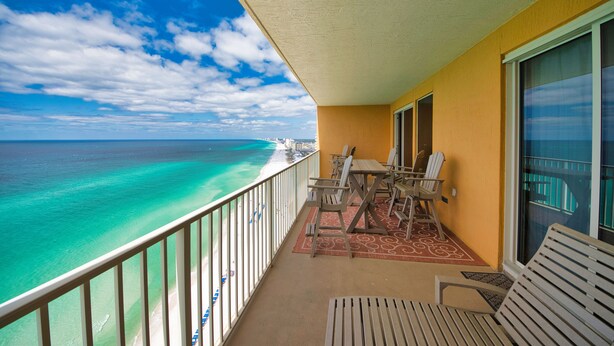 A balcony with a view of the ocean, a table with chairs, and a window. - Treasure Island 2202 (Panama City Beach)