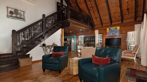 A spacious living area with a wooden staircase, leather armchairs, a flat-screen TV, and a kitchen in the background. - Lakin' it Easy!*Waterfront*Modern*Kayaks*Resort*WIFI*Pets OK (Deep Gap)