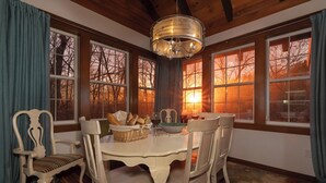 A dining room with a white table, chairs, a chandelier, and large windows with a view of trees. - Lakin' it Easy!*Waterfront*Modern*Kayaks*Resort*WIFI*Pets OK (Deep Gap)