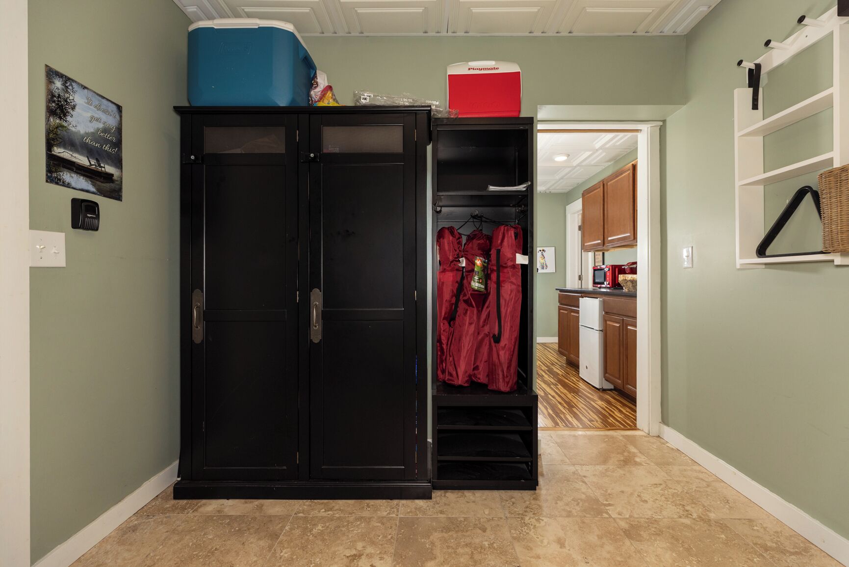 A hallway with a black wardrobe, a red coat hanging, and a Playmate cooler on top.