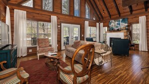 A log cabin interior with a fireplace, wooden furniture, and large windows. - Lakin' it Easy!*Waterfront*Modern*Kayaks*Resort*WIFI*Pets OK (Deep Gap)