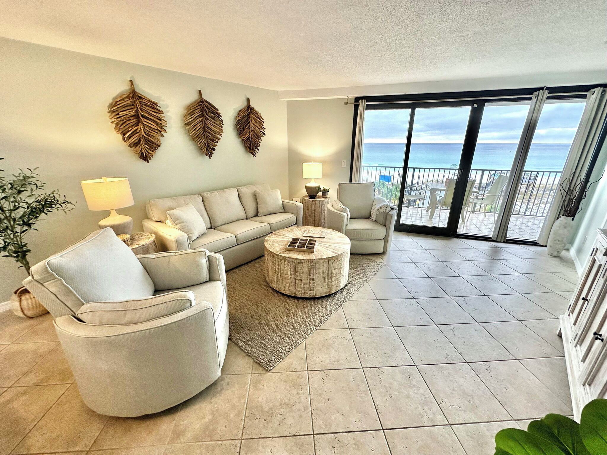 A living room with a sofa, armchairs, a coffee table, and a view of the ocean through large sliding doors.