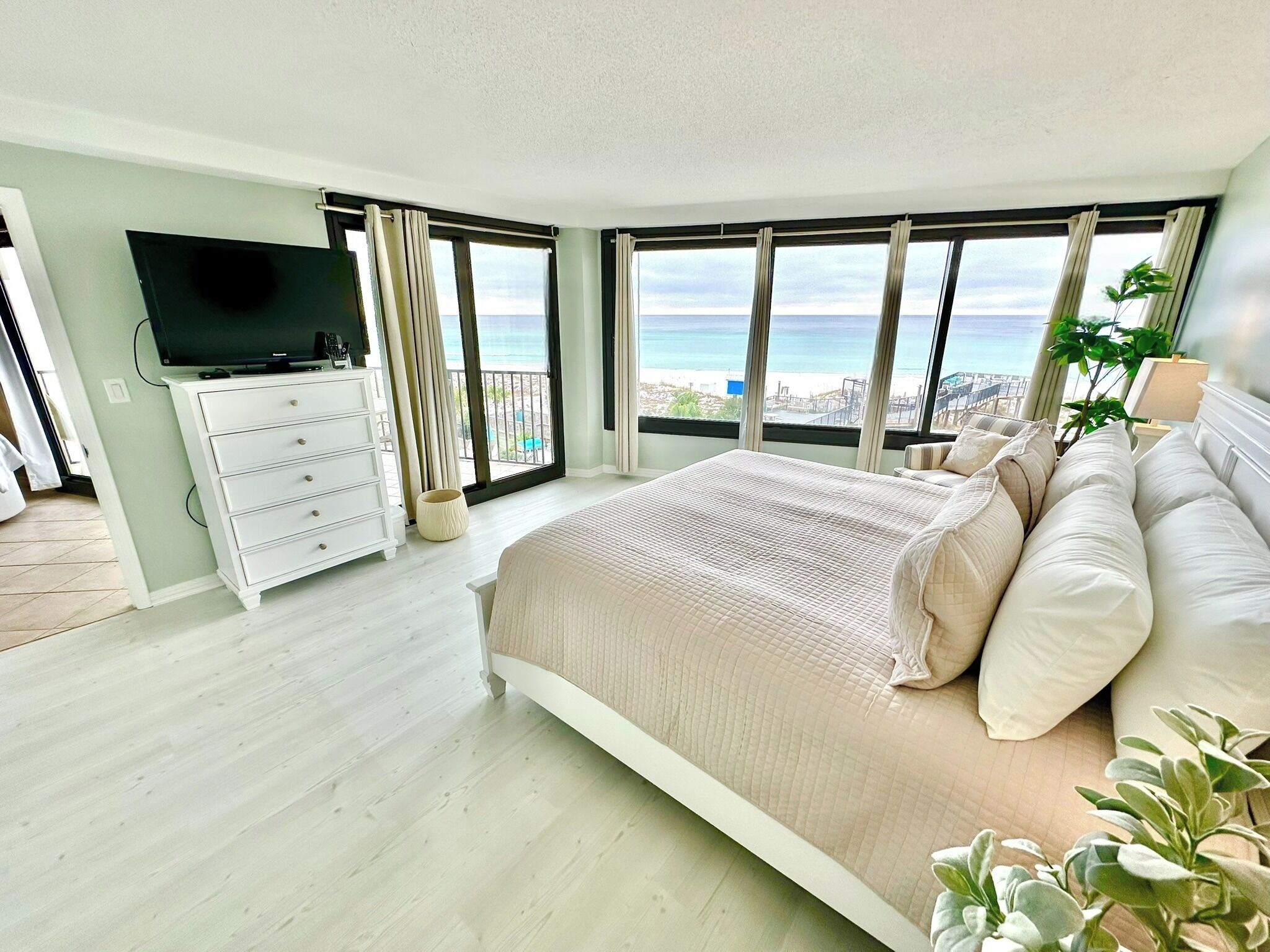 A bedroom with a large bed, a TV, and a balcony with a view of the sea.