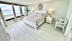 A bedroom with a large bed, a nightstand, a chair, and a view of the beach through a sliding door. - Stunning Beachfront Unit Great Views Golf Cart4045 (Miramar Beach)