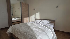 Ein Schlafzimmer mit einem Bett, Holzboden, einem Kleiderschrank und einem Spiegel.