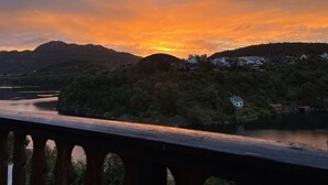 Una vista panorámica de un río con un puente de madera en primer plano, rodeado de colinas y edificios residenciales.