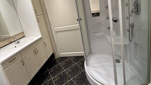 Un baño moderno con ducha de vidrio, lavamanos blanco y tocador con armarios.