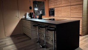 Una cocina moderna con una isla central, taburetes de bar, armarios de madera y electrodomésticos integrados.