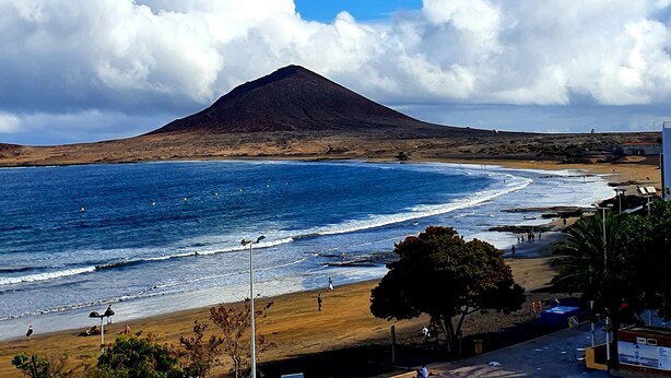 A beach with a mountain in the background, clear skies, and a calm sea.