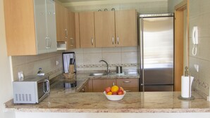 A modern kitchen with wooden cabinets, a stainless steel refrigerator, a microwave, and a fruit bowl on the counter.