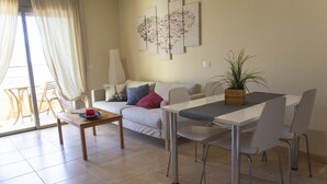 A living room with a sofa, a dining table with chairs, a coffee table, a potted plant, and a painting on the wall.