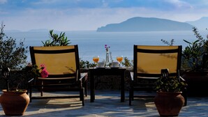 Two chairs facing a table with drinks and a vase, overlooking a body of water and distant land. - Modern hilltop villa with pool near Agios Nikolaos (Vathi)