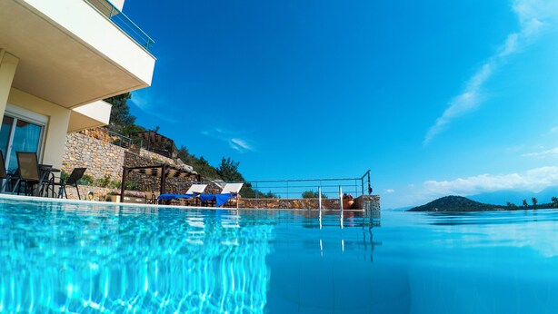 A clear blue pool with lounge chairs and umbrellas, a stone wall, and a view of the sea and mountains. - Modern hilltop villa with pool near Agios Nikolaos (Vathi)