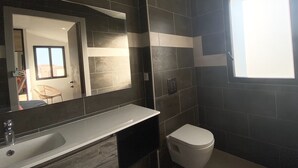 Ein modernes Badezimmer mit dunkel gefliesten Wänden, einer weißen Toilette und einem großen Spiegel über dem Waschbecken.