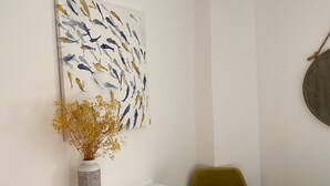 Ein weißes Konsolentischchen mit einer Vase gefüllter getrockneter Blumen, ein grüner Sessel und ein großes abstraktes Gemälde an der Wand.