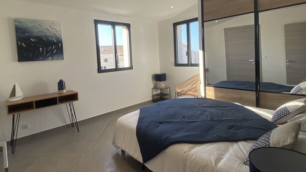 Une chambre à coucher moderne avec un grand lit, une table de chevet, une chaise, une petite table et un grand miroir.