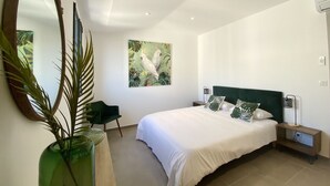 A modern bedroom with a large bed, a green chair, a mirror, and a painting of birds. - Residence Casa U Fornu APT3 (Ile Rousse)