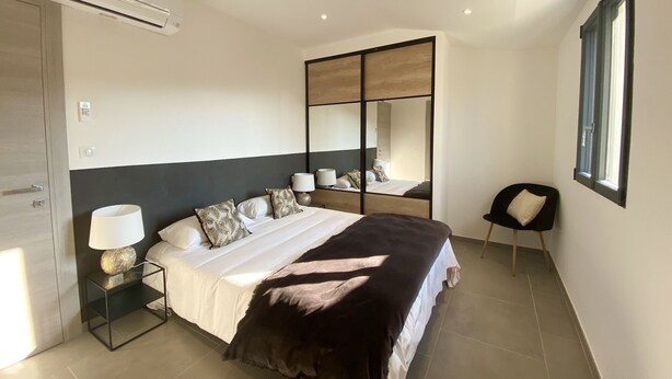 A modern bedroom with a bed, bedside tables, a mirror, and a window. - Residence Casa U Fornu APT3 (Ile Rousse)