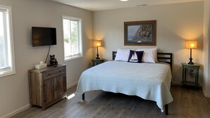 A bedroom with a bed, two bedside lamps, a TV, a dresser, and a painting on the wall. - Lake Front Rental/Downtown Grand Lake
Apt 1 The Chickadee (Grand Lake)