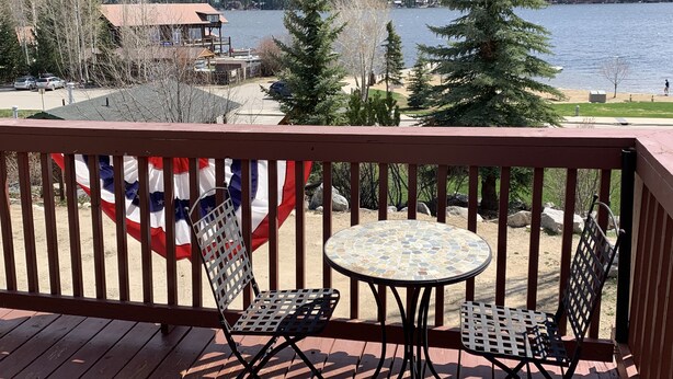A wooden deck with two metal chairs and a small table, overlooking a lake with a forested mountain backdrop. - Lake Front Rental/Downtown Grand Lake
Apt 1 The Chickadee (Grand Lake)