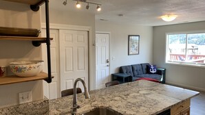 A kitchen with granite countertops, stainless steel sink, and wooden cabinets. There is a dining area with a gray sofa and a small table. - Lake Front Rental/Downtown Grand Lake
Apt 1 The Chickadee (Grand Lake)