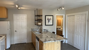 A kitchen with wooden cabinets, a granite countertop, a built-in dishwasher, and a small island with a sink. - Lake Front Rental/Downtown Grand Lake
Apt 1 The Chickadee (Grand Lake)